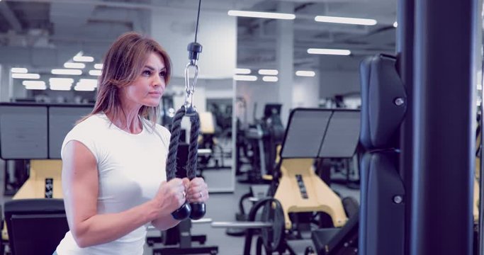 Adult woman doing Exercises for Tricep in fitness gym. Beautiful Woman doing triceps workout. Fitness girl doing triceps cable pushdown exercise in gym