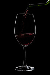 A large glass of red wine is pouring wine from a bottle of red .