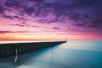 Sunset on the beach with a wooden breakwater, purple tone