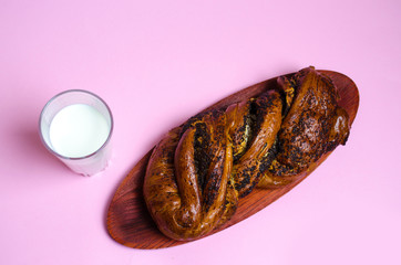 Bun with poppy seeds and a glass of milk on a pink background