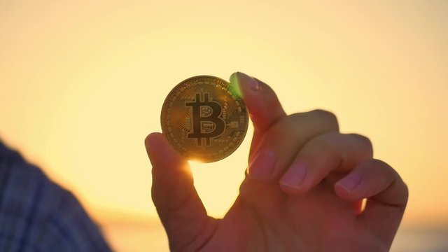 Golden bitcoin coin in hand on a blurred sunset background.