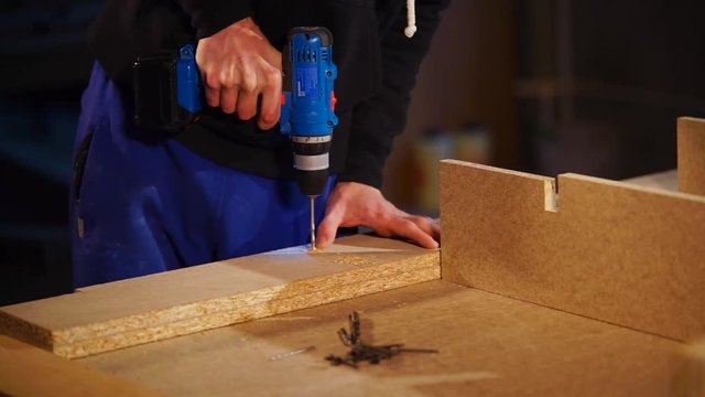 close up shot of the man's hands, who works with the chipboard to then screw in the panel bolts or nails, the person holds the boards with an electric tool