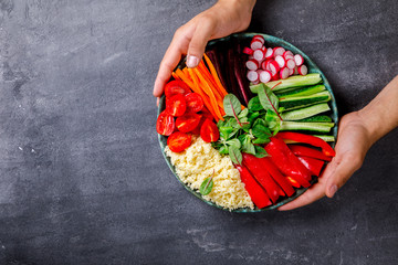 Buddha Bowl Vegetarian on on gray Background in the Hands of Young Men.Raw Vegetables and  in Couscous a one bowl.Food or Healthy Diet concept.Super Food.Copy space for Text. selective focus.