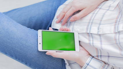 Woman at home relaxing reading on the smartphone with pre-keyed green screen 