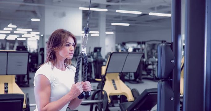 Adult woman doing Exercises for Tricep in fitness gym. Beautiful Woman doing triceps workout. Fitness girl doing triceps cable pushdown exercise in gym