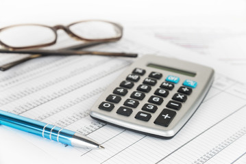 calculator, pen and glasses on a printed financial report with number tables, business concept for...
