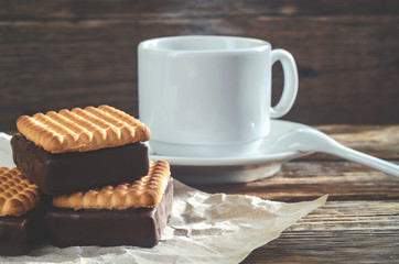 Coffee Cup and a square cookie with chocolate on old wooden table.