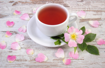 Fototapeta na wymiar Cup of tea and wild rose flower on old rustic board