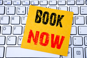 Book Now. Business concept for Reservation Booking written on sticky note paper on the white keyboard background.
