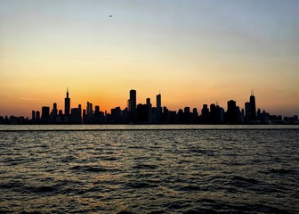 Evening sunset over Chicago silhouettes the skyline, as seen from Lake Michigan, which is glowing with orange sunlight.
