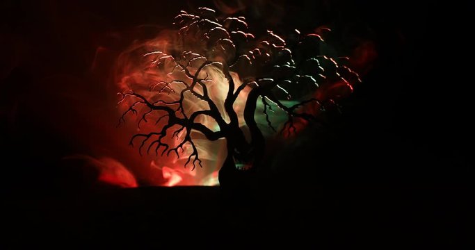 Silhouette of scary Halloween tree with horror face on dark foggy toned background with moon on back side. Scary horror tree with zombie and monster demon faces.