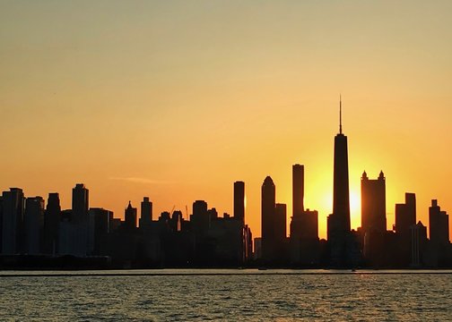 Sun sets over Chicago skyline silhouette, as seen from Lake Michigan, which is glowing with orange sunlight.