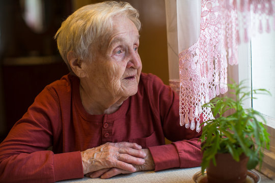 An elderly woman looks out the window.