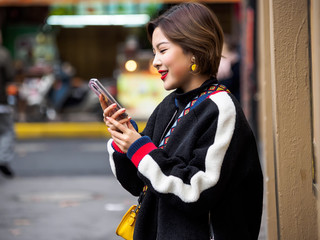 Beautiful young brunette woman wearing a black coat in autumn city. Outdoor fashion portrait of glamour young Chinese cheerful stylish lady in street. Emotions, people, beauty and lifestyle concept.
