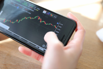 Woman hand trading stock with mobile phone on coffee shop background