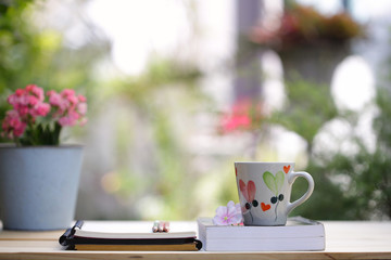 White mug with heart pattern and book with pink fairy rose