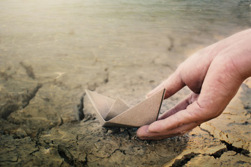 Hand holding paper boat on cracked ground, concept drought