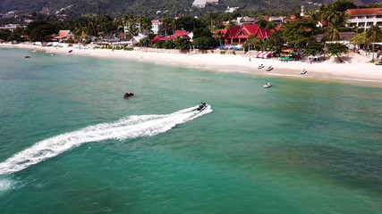 Obraz premium Aerial view of white sand beach and jet ski on the blue lagoon aqua sea. Aerial bird's eye view of jet ski cruising in high speed in turquoise clear water sea