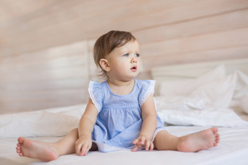 Fototapeta premium Pretty little baby girl sits on a bed and looks to side