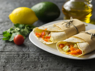 Two vegetable roll tortilla from wheat flour in white bowl and lemon and avocado on a wooden table with herbs.