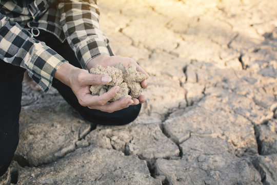 Hands holding soil on cracked dry ground, concept drought and crisis environment