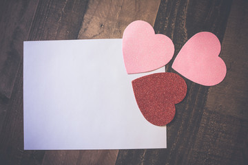 White paper on wooden table with three sparkly cutout hearts 