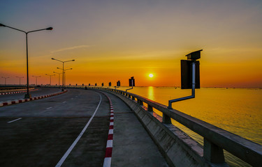 Curved coastal road with street lamp and orange sky at sunset in Chonburi, Thailand.