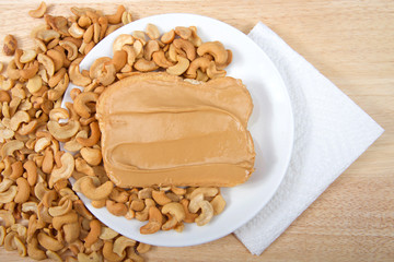 Cashew butter spread on bread on a white plate surrounded by cashew nuts. Cashews are a good source of plant protein, contain no cholesterol and are low in saturated fat.