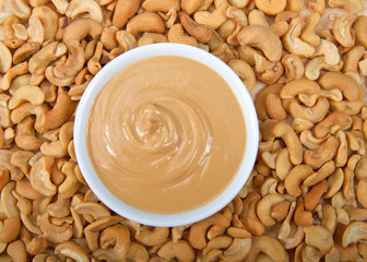 White bowl with fresh cashew butter surrounded by cashew nuts. Cashews are a good source of plant protein, contain no cholesterol and are low in saturated fat.