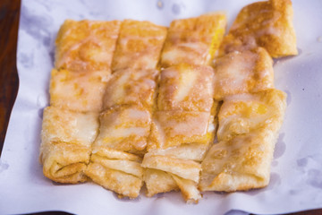 Roti with egg and sprinkle with white sugar and sweetened condensed milk, cut into square pieces, placed on white paper.