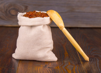 Bag with red Cargo rice and spoon on wooden table.
