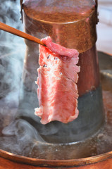  Thin slices of beef  in chopsticks over hot pot with smoke   