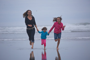 Happy Family Concept. Beautiful Young Mother run with two daughters on the Beach at Cannon Beach Oregon USA, Pacific Ocean, West coast, Vacation Time, Big Ocean's waves at the Background 