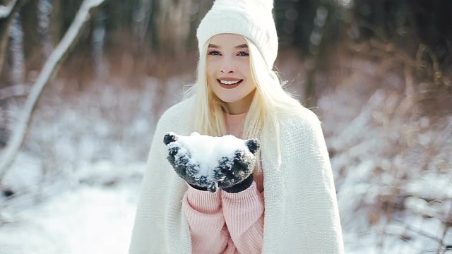Attractive young blonde woman blowing snow flakes at camera