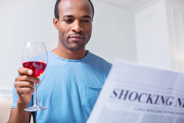 Interesting news. Positive joyful nice man sitting at home and having wine while reading articles