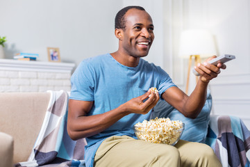 Favourite entertainment. Delighted happy positive man eating popcorn and holding a remote control...