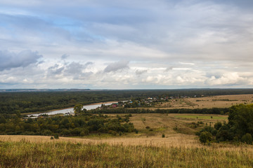 Fototapeta premium View from the height on the field, trees and river in the distance in autumn day