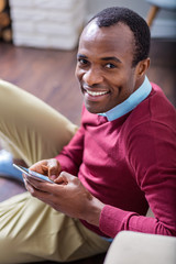 Modern gadget. Cheerful nice handsome man smiling and looking at you while using his mobile device