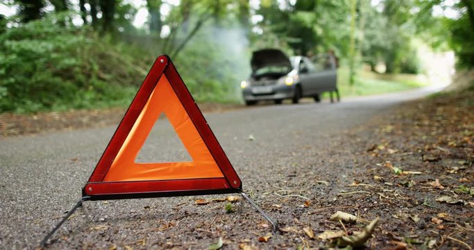 4K Woman gets out of broken down car on country road, red warning triangle in foreground