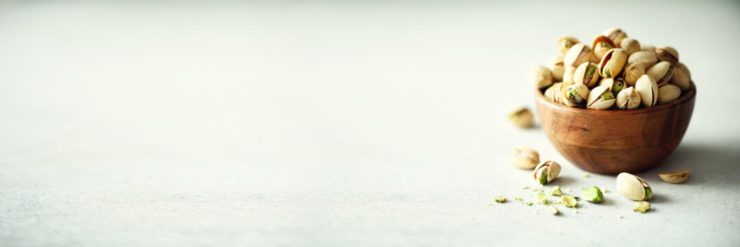 Green salted pistachios in wooden bowls on light concrete background. Copy space for your text. Healthy nuts snack. Banner