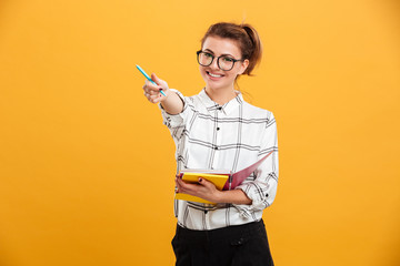 Photo of attractive woman posing with textbooks in hands and showing pen at camera, isolated over...