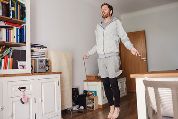 Young man in sportswear jumping rope in his living room