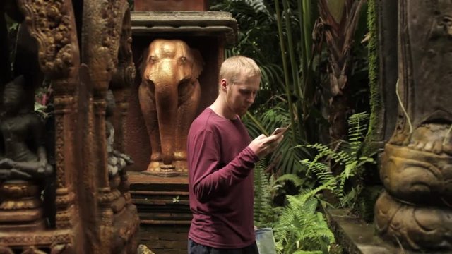 tourist with a phone walks in the park with statues in the style of Bali
