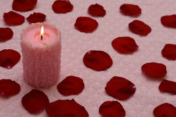 Burning candle and red rose petals