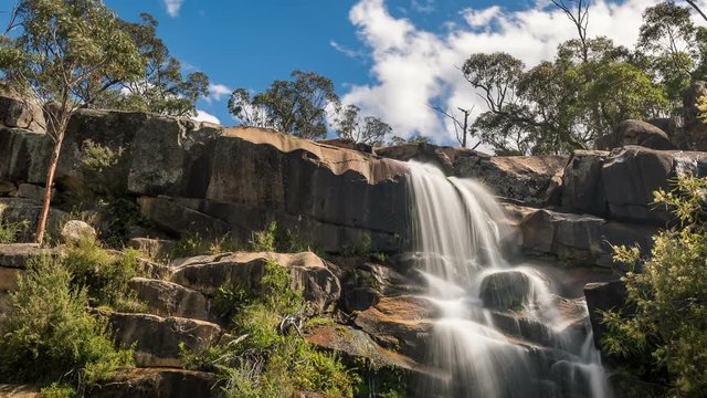 Timelapse of a beautiful waterfall flowing down a rock face on a warm sunny day.