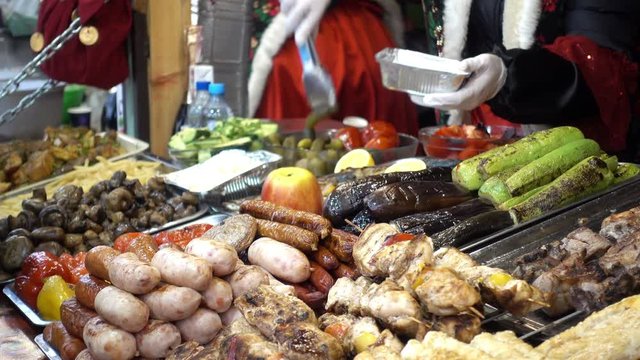 4K view of the sale of food in street food stores. The seller puts the food on the plate. Various ready-made meals and snacks on the counter.