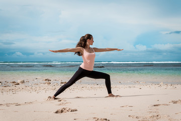 Fototapeta na wymiar Young woman practices yoga on a beach at sunrise in front of ocean. Morning gymnastic. Rise hands.