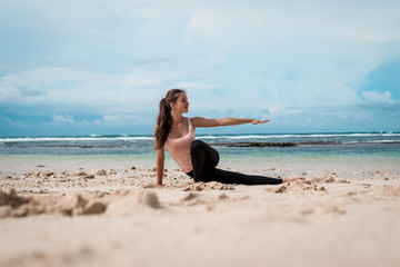 Fototapeta na wymiar Sporty woman practicing yoga on the beach at sunrise. Healthy lifestyle.