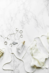 Overhead view of female lace lingerie, perfume and jewelry items on white marble background. Top view, text space. Monochromatic concept