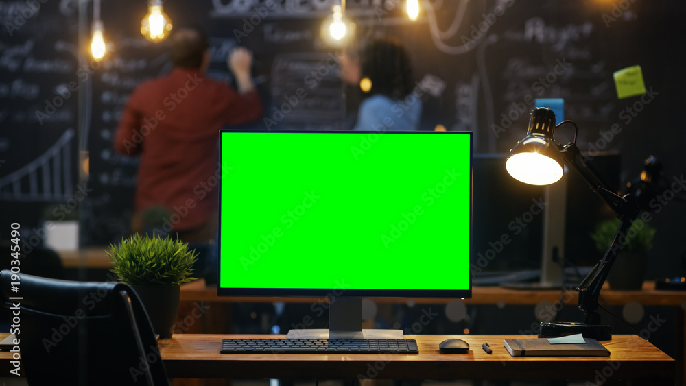 Poster personal computer with mock-up green screen monitor stands on the office desk, in the background peo